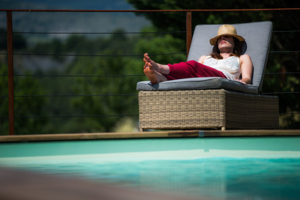Femme allongée sur un transat en bois à côté de la piscine avec un chapeau sur la tete