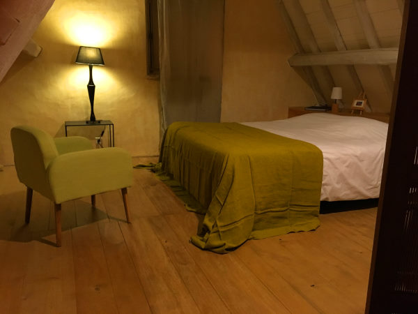 Chambre double sous pente avec un couvre lit vert olive un fauteuil vert olive