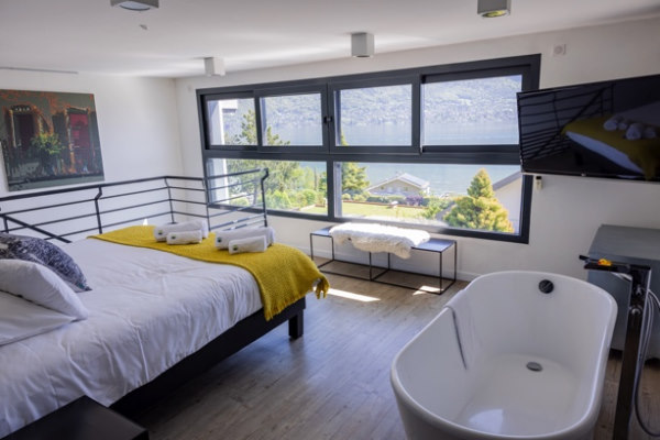 Chambre double avec une fenêtre panoramique sur le lac. A côté du lit une belle baignoire design