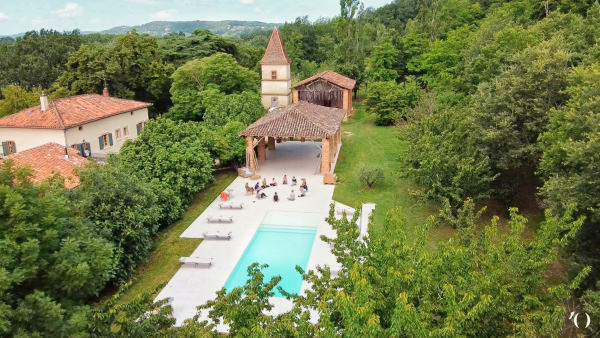 écolodge occitanie -  L'ostalas vue du cial avec la piscine, un groupe de personne entrain de méditer assis en cercle au bout de la piscine et derrière le dojo