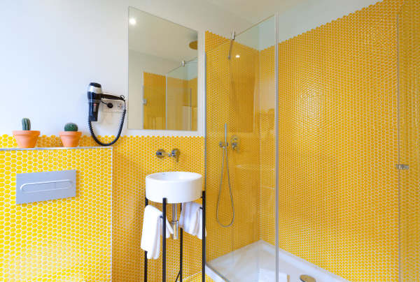 Salle de bain dans les tons jaune et blanc avec une grande douche à l'italienne et une vasque ronde sur pieds noirs