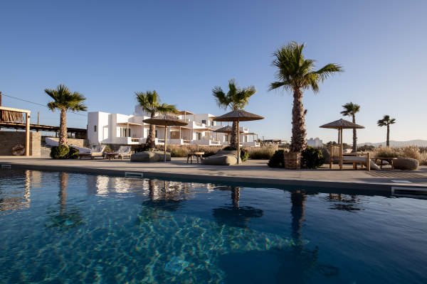 hotel de charme paros - photo prise de la piscine de l'autre côté les transats et les palmiers et derrière le batiment blanc de l'hotel