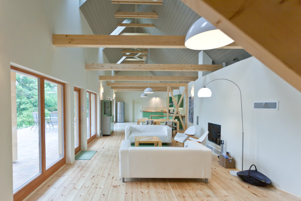 irota-ecoLodge - Vue intérieure d'un grand salon à la décoration minimaliste et claire avec une cuisine ouverte et de grande menuiseries coulissantes en bois donnant sur une grande terrasse