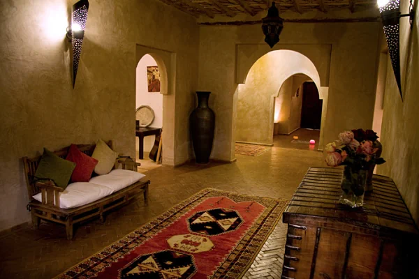Hall d'entrée de l'établissement avec des murs à la chaux aux couleurs ocres, un tapis marocain traditionnel par terre et un banc avec des coussins blancs à gauche