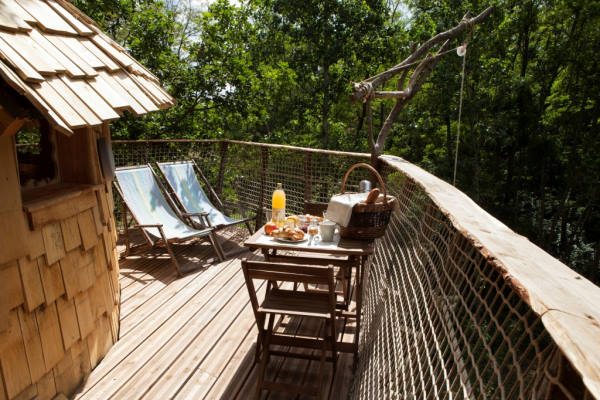 hébergement insolite touraine - Table du petit dejeuner dressée sur une terrasse en bois perchée en haut d'un arbre. deux chiliennes sont également dépliée face au soleil
