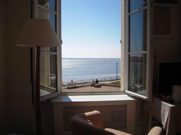 Photo prise de l'intérieur d'une chambre avec la fenetre grande ouverte et vue sur la mer, le ciel bleu et le soleil