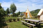 Photo prise dans le camping avec une table de pique nique en bois et une tente orange et jaune derrière