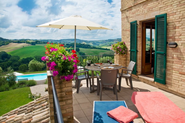Photo prise sur une terrasse avec du mobilier de jardin et un parasol ouvert. En contrebas on aperçoit la piscine.