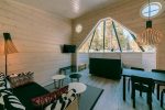 Laponie - Pyha Igloo. Photo a l'intérieur de l'igloo avec les murs recouverts de bois, un espace salon, une table à manger et le lit sous le dome de verre