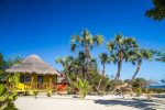 Bungalow en bois jaune vif qui contraste avec le blanc su sable, la vert de la végétation et le bleu éclatant du ciel