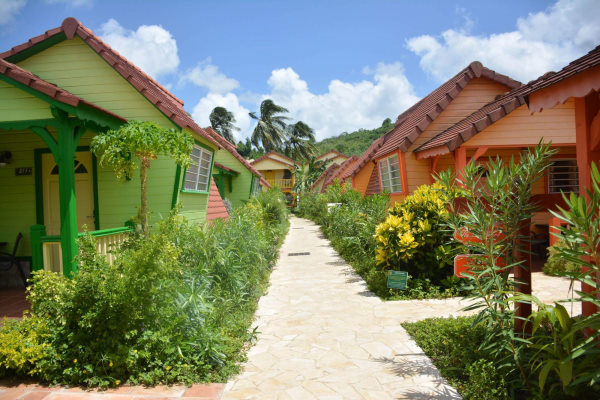 Martinique - Hotel bambou. Allée de l'hôtel avec de chaque côté des bungalow en bois coloré vert ou orange. Les allées sont également bordées de végétation