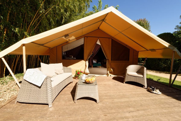 Photo d'une tente de glamping de face de couleur beige avec sa grande terrasse amenagée de bain de soleil