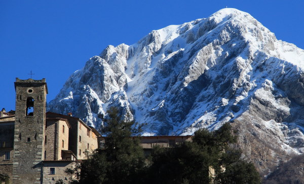 Pania Forata Hostel. Vue du village en pierre en contre plongée et derrière une grande montagne avec le sommet enneigé