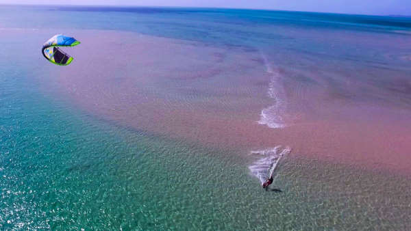 Kitesurf sur une eau translucide avec des reflets rosés