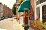 Eco-hôtel Fevery Bruges - Photo de la devanture fleurie avec des murs en briques rouges, des menuiseries blanches et un auvent vert