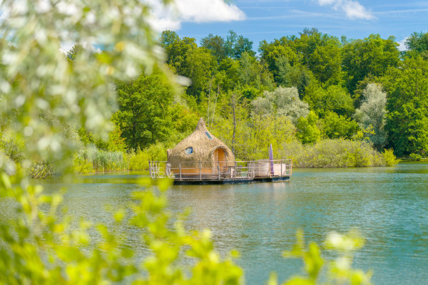Les grands lacs - cabane en bois sur une plateforme flottante au milieu du lac avec toit en paille