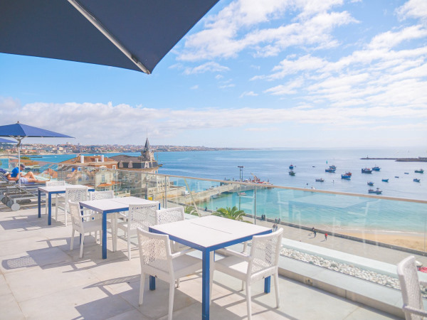 Hotel baia cascais - photo prise de la terrasse de l'hotel face à la mer. La terrasse est amenagée le long de la balustrade en verre de table de restaurant et au fond il y a des transats