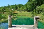 Le Camp. Photo prise sur le ponton de la piscine naturelle. A droite sur les rives un fauteil pour se relaxer et au fond sur les pentes de la coline on aperçoit une tente de glamping