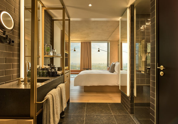 QO - Photo en perspective prise depuis la salle de bain avec la faience noire qui donne directement dans la chambre avec le lit 2 places et 3 grandes fenetres
