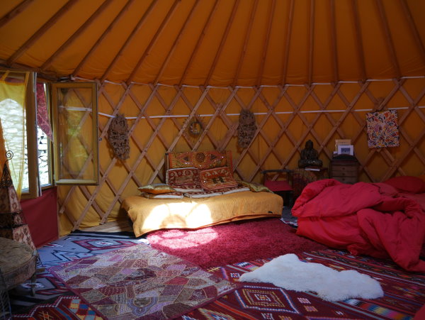 weekend en cevennes - Interieur de la yourte dans les tons jaunes et rouge avec beaucoup de tapis et une fenetre ouverte