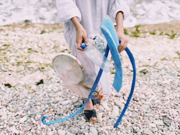 Une femme sur une plage tenant dans ses mains des déchets plastiques qu'elle a ramassé