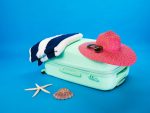 vacances zéro déchet - 6serviette bleue et blanche placée à côté d'un chapeau rose tous les deux posés sur une petite valise