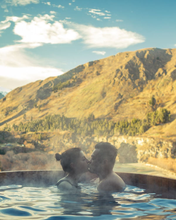 nature weekend for two: a couple kissing in an outdoor hot tub with a spectacular view