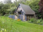 cabane grise avec des volet bleu au milieu d'une pelouse tres verte