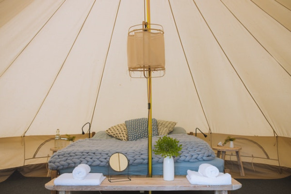 Photo of the interior of a glamping tent with a small table at the entrance with a mirror and towels, behind the double bed with a pastel blue blanket and pillows