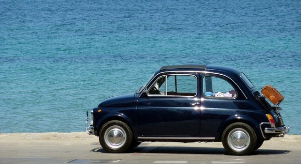 Navy blue Fiat 500 with a wicker basket on the trunk parked along the sea