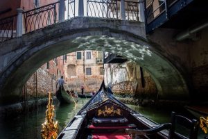 Photo taken from a gondola passing under a bridge in Venice. in front of her two other gondolas with their gondolier