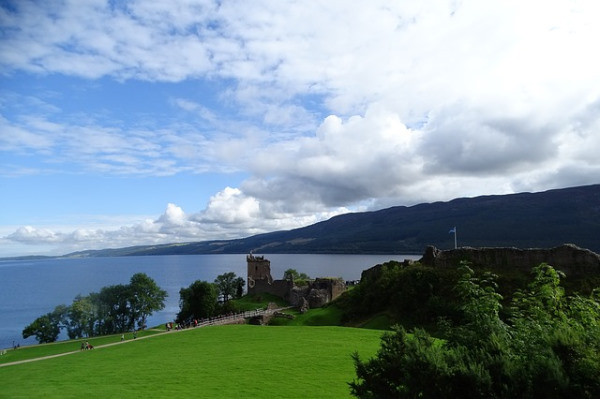 Photo du loch ness prise depuis une colline avec au premier plan les ruines d'un chateau et derrière le lac