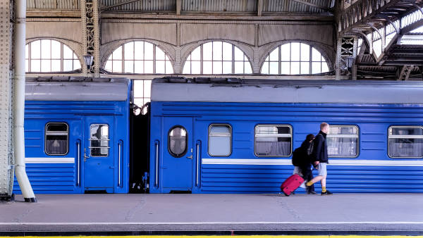 Eco-responsible travel - Man with a red suitcase along the platform of the station where a blue train is parked