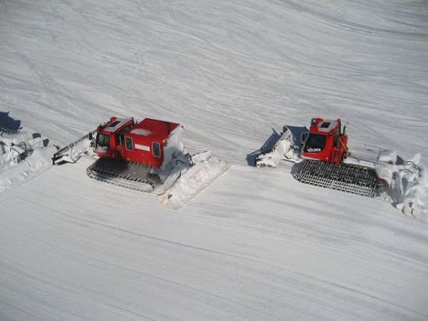 deux dameuses rouges en action sur une étendue de neige fraiche