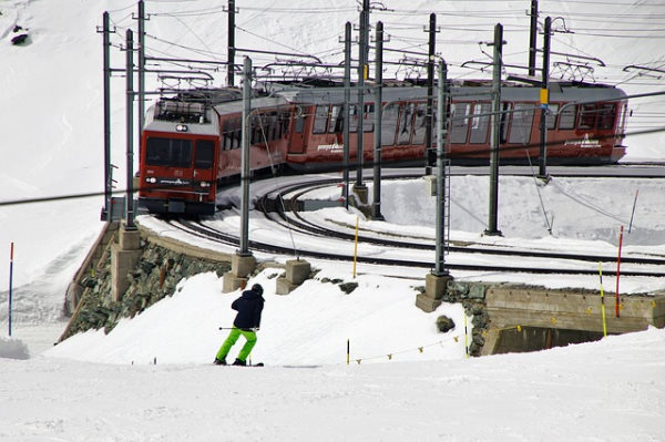 station de ski écologique - un skieur avec un pantalon vert entrain de descendre une piste de ski pendant qu'on voit un train passé devant lui