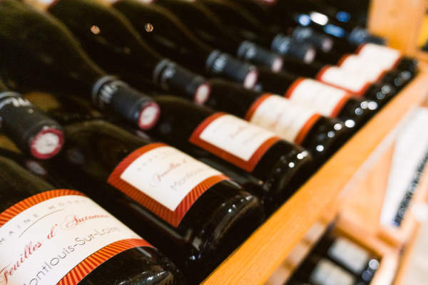 Bouteilles de vin avec une etiquette blanche bordée de rouge rangées sur des étagères en bois