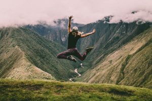 Femme de dos sautant de joie face à un paysage de montagne grandiose