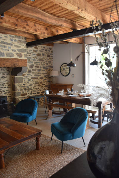 Salle à manger avec un grande table en bois pour le diner, 2 fauteuils crapaud bleu canard et une grande cheminée en pierre