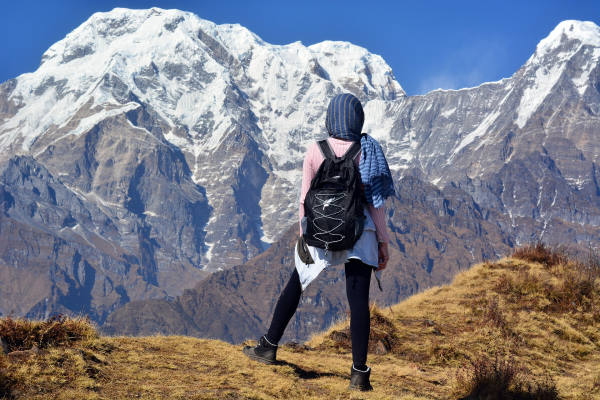 plus beaux treks du monde - Femme de dos avec sac à dos noir face à une montagne enneigée