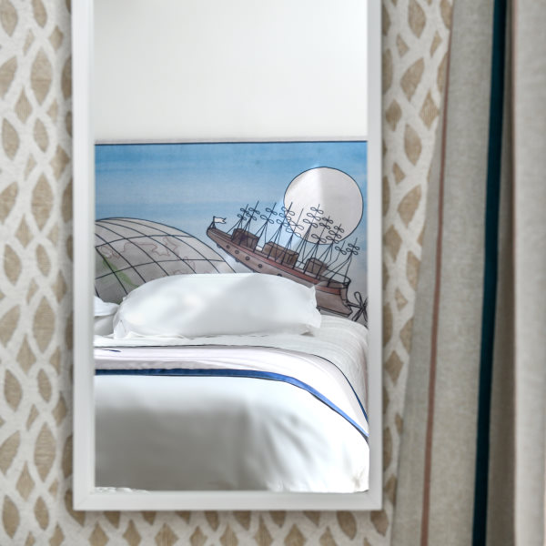 Photo d'un lit prise au travers d'un miroir blanc accroché sur une tapisserie beige et blanche