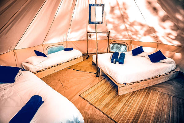 glamping finistère - intérieur d'une tente de glaping pour 4 personnes avec un lit double et 2 lits simples. Sur chaque lit  une couette blanche et des cousins et serviettes bleus