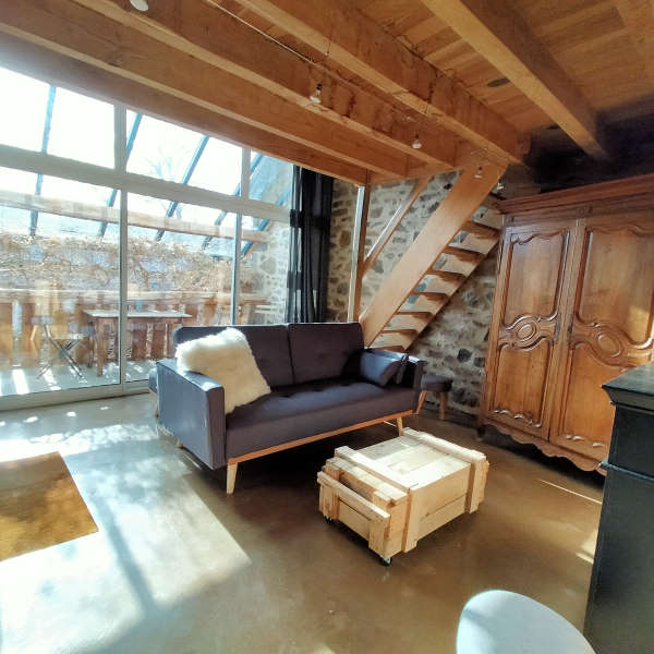 maison d’hôtes puy de dôme - salon avec canapé gris et caisse en bois servant de table basse installés devant une grande baie vitrée