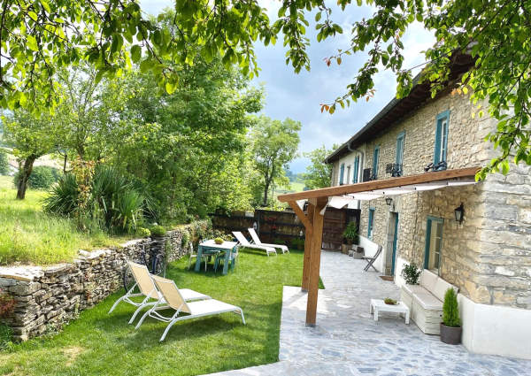 Maison en pierre avec des contours de fenetres bleus, sa cours privative et son jardin equipé de mobilier extérieur blanc