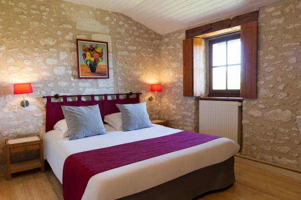 hotel de charme châtellerault - lit double devant un mur en pierre avec dessus de lit violet